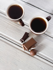 Two mugs of hot black aromatic coffee and a snack in the form of chocolate