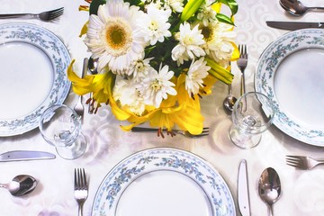 Elegant dining set on a white tablecloth in a fancy restaurant with arranged flowers in a vase on the table