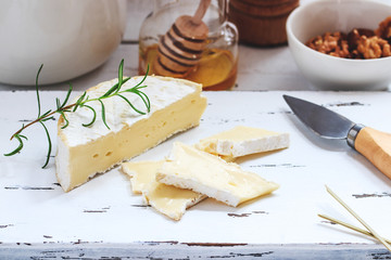 Cheese plate served with crackers, honey and nuts. Camembert on white wood serving board over white texture background. Appetizer theme.