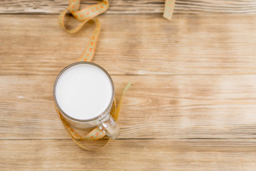A glass of milk (kefir) and a measuring tape on a wooden background. The concept of diet, weight loss.