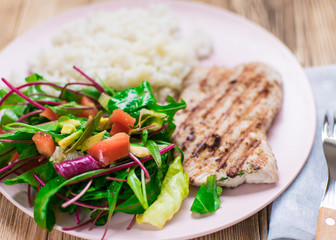 Grilled meat, boiled rice and vegetable salad on a wooden background.