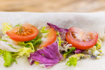 Preparation of a roll of pita bread and fresh vegetables on a wooden background. The concept of healthy eating.