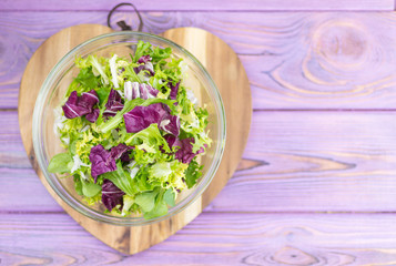 A fresh salad of greens on a wooden background in the form of a heart. Vegetarian food. Diet.