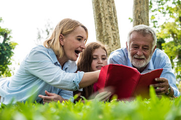 Fototapeta premium Activities in the family, Father, mother and daughter reading a book while laying down on green grass in a park