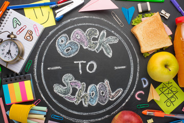 The inscription back to school, on a school board with handles, chalk, an alarm clock, and school breakfast