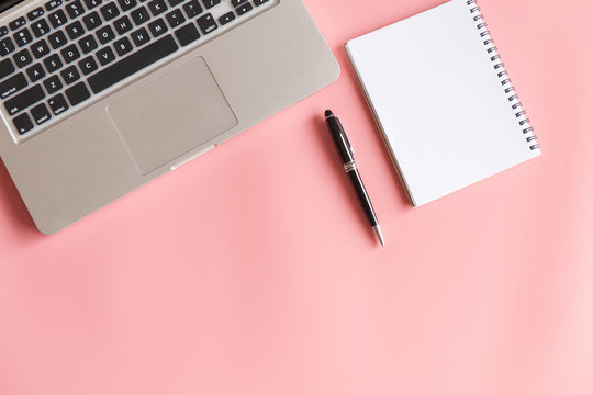 Top View of a Notebook, pen, Computer laptop and Writing Stationery on pink and blue pastel color background.