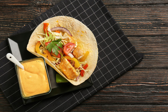 Plate with tasty creamy sauce in bowl and fish taco on wooden table