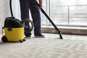 Male worker cleaning carpet with vacuum indoors