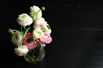 Glass vase with beautiful ranunculus flowers on black background