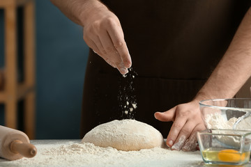 Fototapeta premium Man sprinkling flour over dough on table in kitchen
