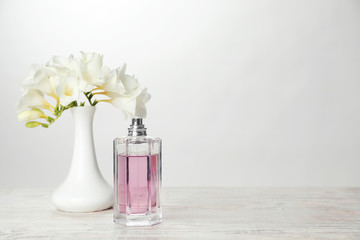 Bottle of perfume and vase with flowers on table against light background