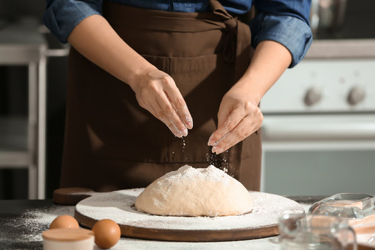 Woman sprinkling flour over dough on table in kitchen