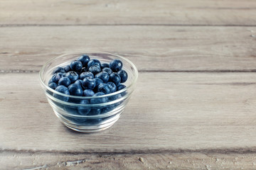 Fototapeta na wymiar Fresh blueberries in small transparent glass bowl placed on wood desk.