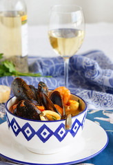 french soup Bouillabaisse with mussels, clams, langoustines, squid, cod, trout in white bowl with blue patterns