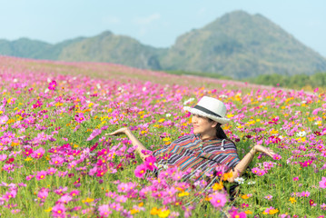 Fototapeta na wymiar Traveler asian woman relax and freedom in beautiful blooming cosmos flower garden. Travel and Lifestyle Concept.