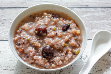 Eight Treasure Congee on traditional chinese festive porridge, mixed from eight ingredients: red beans, lotus seeds, peanuts, dates, pine nuts, lily, almond and walnut on white wooden table, top view