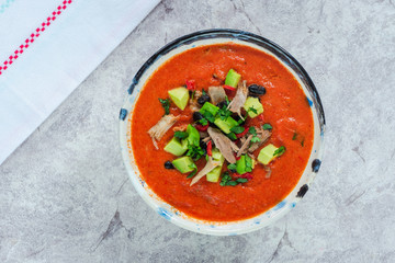 Spicy Mexican roast chicken and tomato soup with black beans,  garnished with fresh avocado - top view