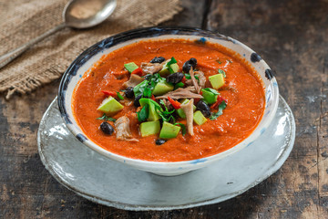Spicy Mexican roast chicken and tomato soup with black beans,  garnished with fresh avocado