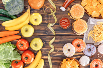 top view of assorted junk food, fresh fruits with vegetables and measuring tape on wooden table