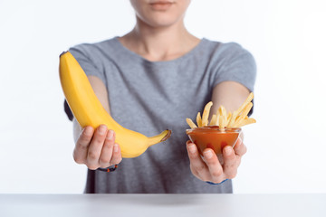 cropped shot of girl holding ripe banana and ketchup with french fries