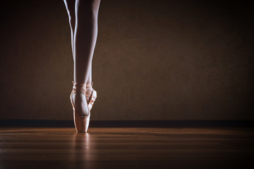 The girl in Pointe stands on the wooden floor in the contour light