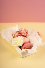 Several pink macaroons cakes one of which is bitten are placed in a gift box with wrapping paper with buds of a rose and a carnation