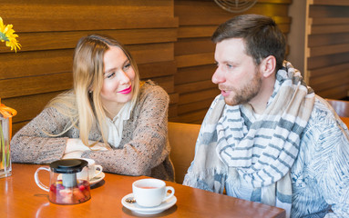 Happy young couple is talking and drinking coffee and smiling while sitting at the cafe.