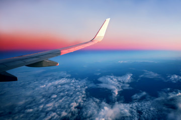 Naklejka na ściany i meble Airplane flying above clouds at pink sunrise
