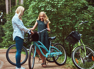 Fototapeta na wymiar Portrait of a mother and daughter with a blonde hair on a bicycle ride with their cute little spitz dog in the park.