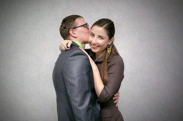 Young business couple is kissing and smiling isolated on gray background. Loving relationships at work concept.