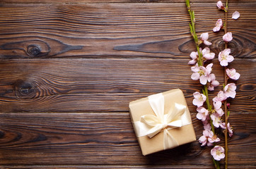 Bunch of spring flowering branches with many pink blossoms on dark brown wooden background. Rustic composition, tree flowers on vintage wood table, present craft paper. Close up, copy space, top view.