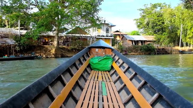 INLE LAKE, MYANMAR - FEBRUARY 18, 2018: The wooden canoe boat floats along the Indein creek with village houses, agricultural lands and forests on its banks, on February 18 in Inle Lake.