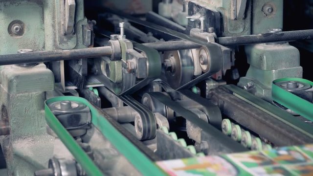 Printed magazines are going along the conveyor belt when mechanical razors cut off their extra sides