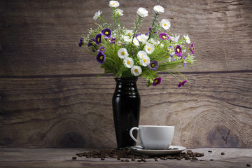 Flowers in a black jug and a cup of morning coffee.
