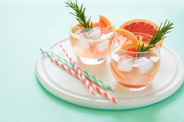 Refreshment grapefruit cocktail with rosemary on white wooden board. Healthy citrus summer drink. Mint color background