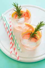 Refreshment grapefruit cocktail with rosemary on white wooden board. Healthy citrus summer drink. Mint color background