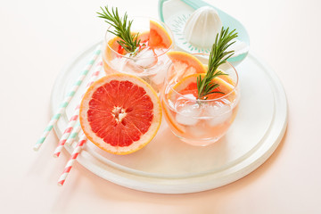 Refreshment grapefruit cocktail with rosemary on white wooden board. Healthy citrus summer drink. Pink background