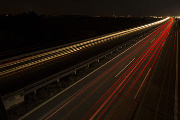Motion blurred light tracks glowing to the darkness of highway traffic to the city just after sunset. Creative long time exposure photography.