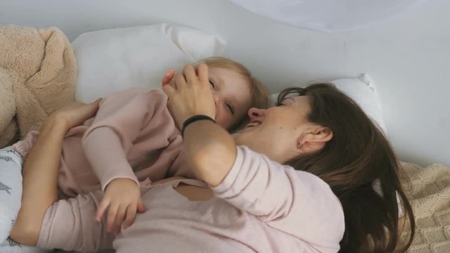 Mother plays with little daughter on the bed
