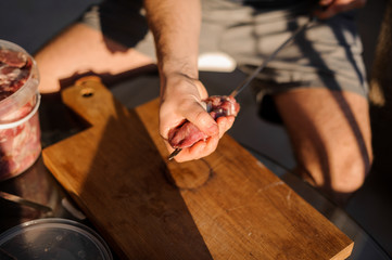 Man string a large meat pieces on the skewer