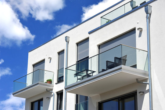 Moderne Balkone, verglast mit Metall-Geländer an Neubau-Hausfront mit Flachdach, Wasserkästen, Regenfallrohren und Edelstahl-Attika