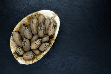 Pecan Nuts with the Nutshell in Eco Natural Banana Leaf Plate on Black Stone Background Surface with Free Space