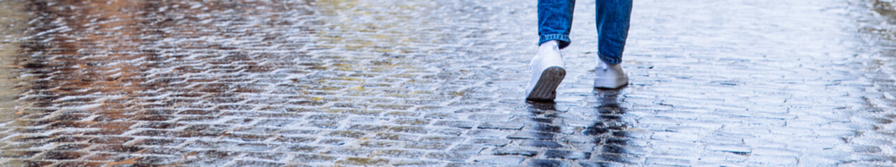 woman in white sneakers walk by wet cobble. copy space. wide angel