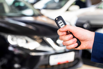 Male hand holds car key in car showroom