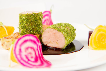 Roast pork tenderloin with crispy potato bread, marinated beetroots and green pepper sauce on a plate on a white background