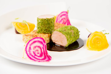Roast pork tenderloin with crispy potato bread, marinated beetroots and green pepper sauce on a plate on a white background