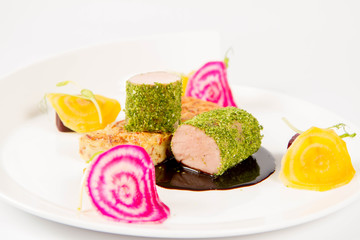 Roast pork tenderloin with crispy potato bread, marinated beetroots and green pepper sauce on a plate on a white background
