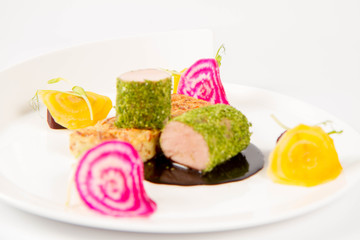Roast pork tenderloin with crispy potato bread, marinated beetroots and green pepper sauce on a plate on a white background