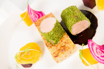 Roast pork tenderloin with crispy potato bread, marinated beetroots and green pepper sauce on a plate on a white background