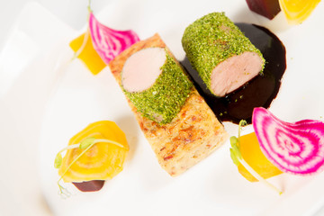 Roast pork tenderloin with crispy potato bread, marinated beetroots and green pepper sauce on a plate on a white background